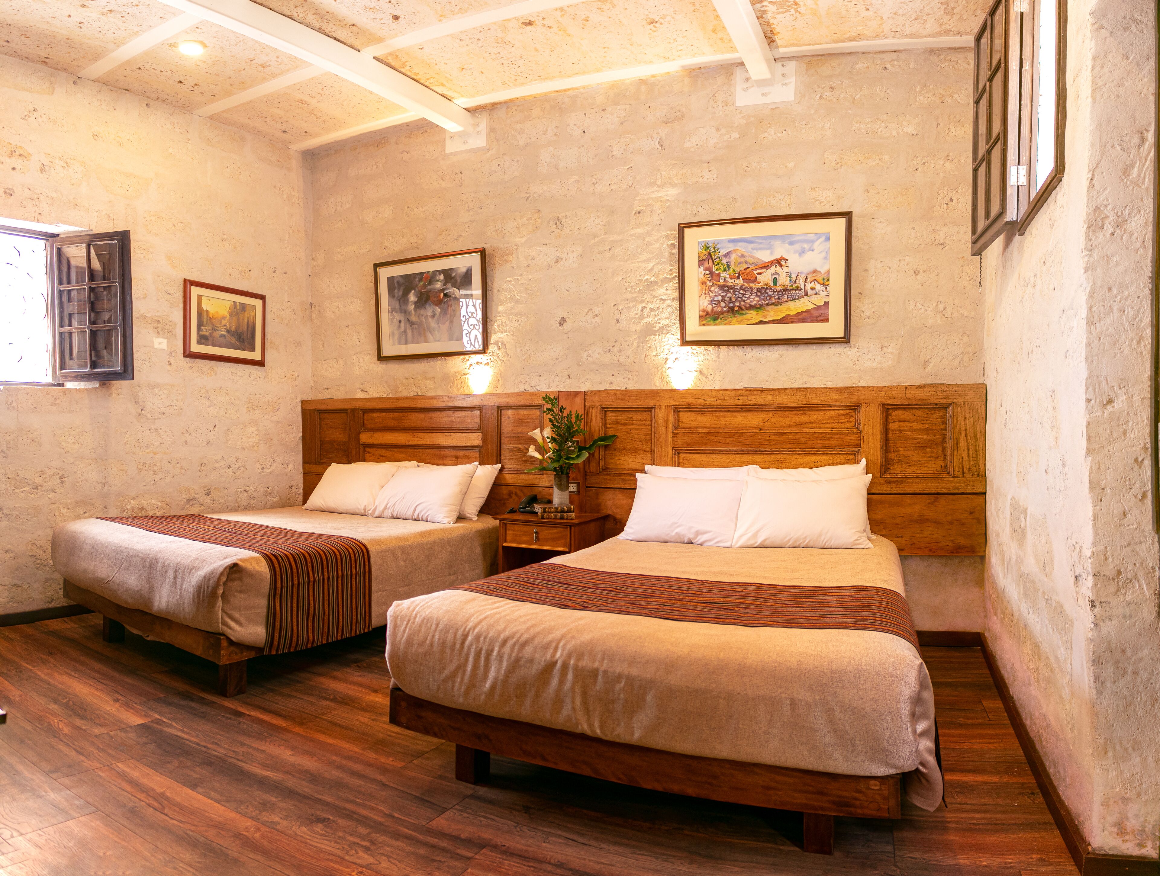 Una habitación con dos camas de madera, cada una con cabecero de madera, una mesita de noche con lámpara y un cuadro en la pared.