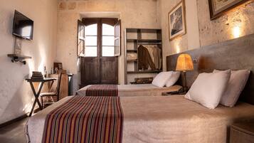 A room with two beds, a wooden headboard, a desk with a chair, a shelf with clothes, and a painting on the wall.