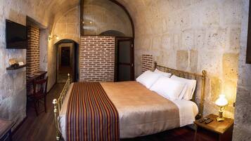 A bedroom with a brick wall, a wooden bed, a bedside table with a lamp, and a TV mounted on the wall.