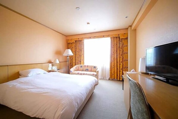 A hotel room with a large bed, a desk with a television, a chair, and a window with curtains. - Yuzawa Royal Hotel (Yuzawa)