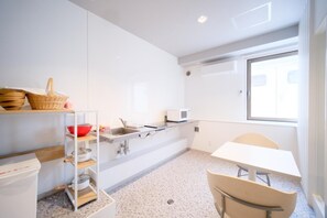 A modern kitchen with white cabinets, a sink, a microwave, and a window providing natural light. - Yuzawa Royal Hotel (Yuzawa)