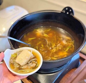 A pot of soup with noodles and a dumpling on a stove.