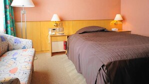 A hotel room with a bed, a bedside table with a lamp, a small desk with a computer, and a patterned sofa. - Yuzawa Royal Hotel (Yuzawa)