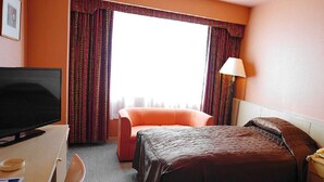 A hotel room with a bed, a desk with a television, a chair, and a window with curtains. - Yuzawa Royal Hotel (Yuzawa)