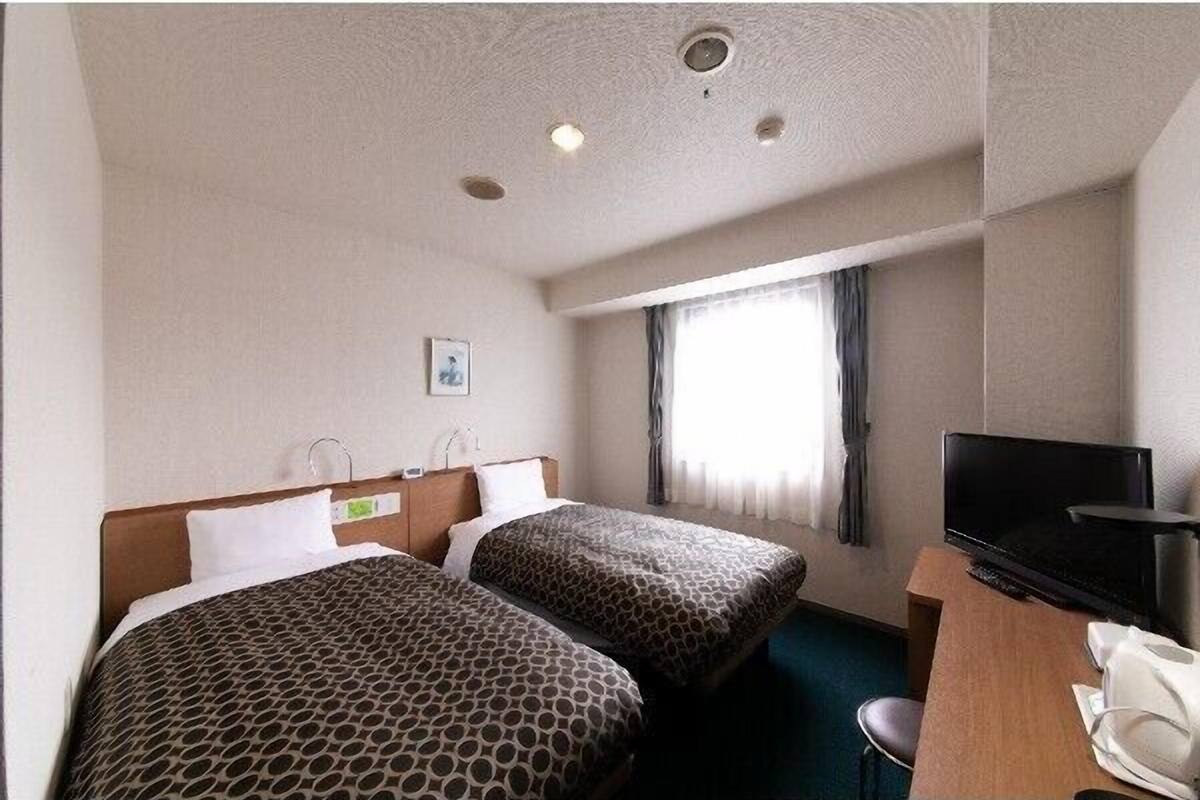 A hotel room with two beds, a desk, a television, and a window with curtains.