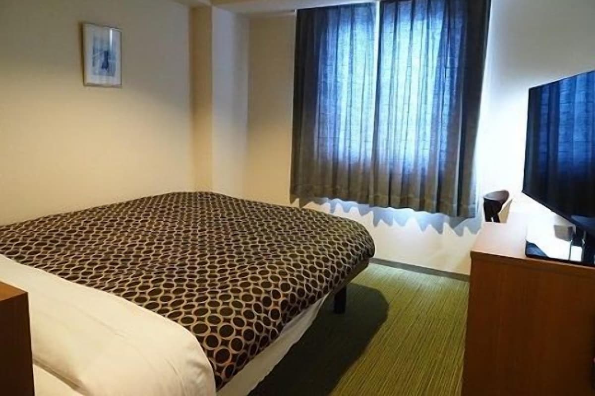 A hotel room with a bed, a desk, a chair, and a window with curtains.