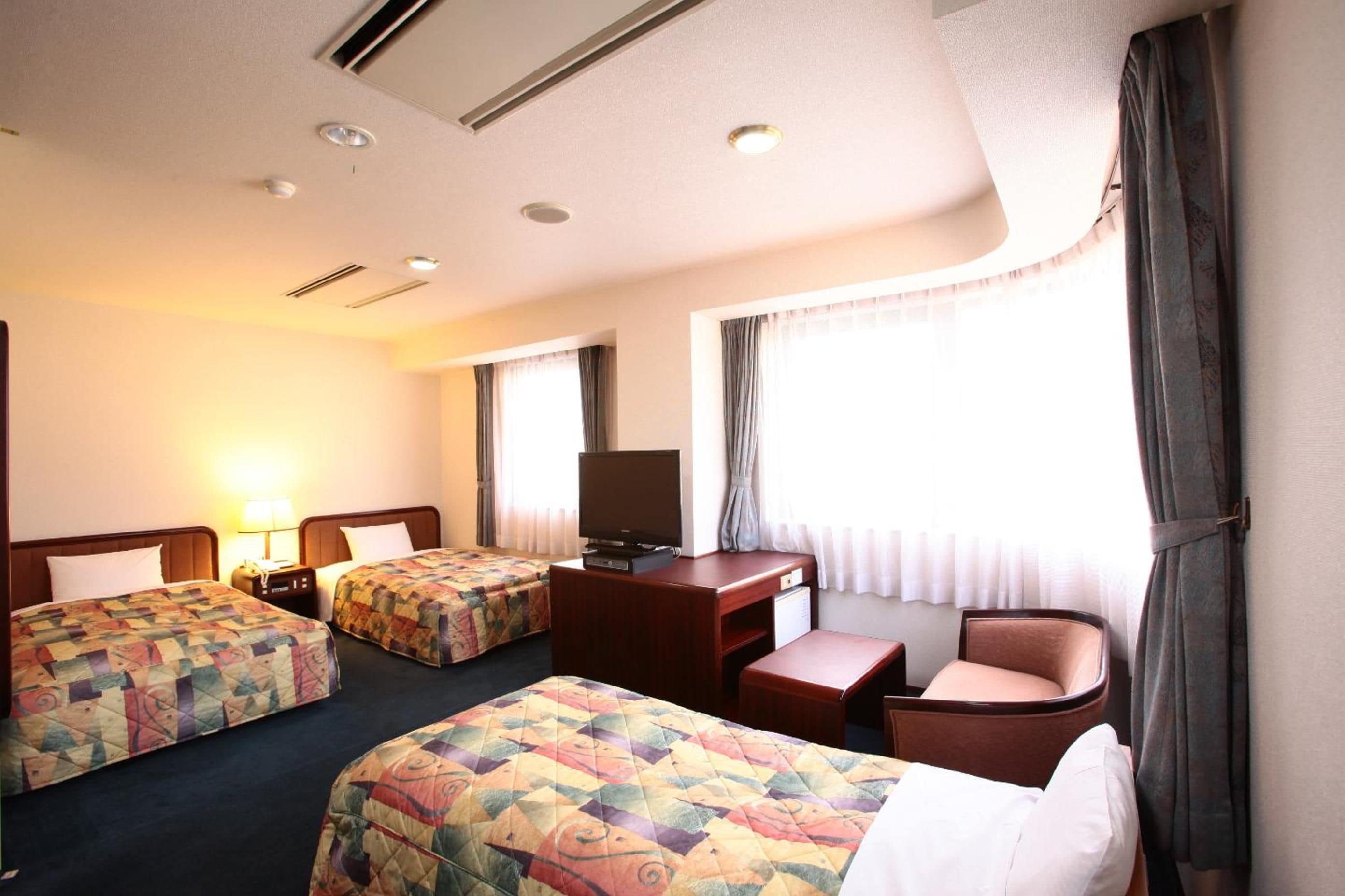 A hotel room with two beds, a desk, a chair, a television, and a window with curtains.