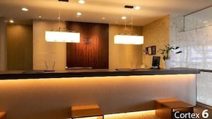 A reception area with a wooden reception desk, two pendant lights, and a plant. - Hotel Ermou Regency (Shimizu)