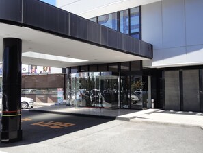 Una entrada de edificio moderna con puerta de vidrio y un bolardo negro.