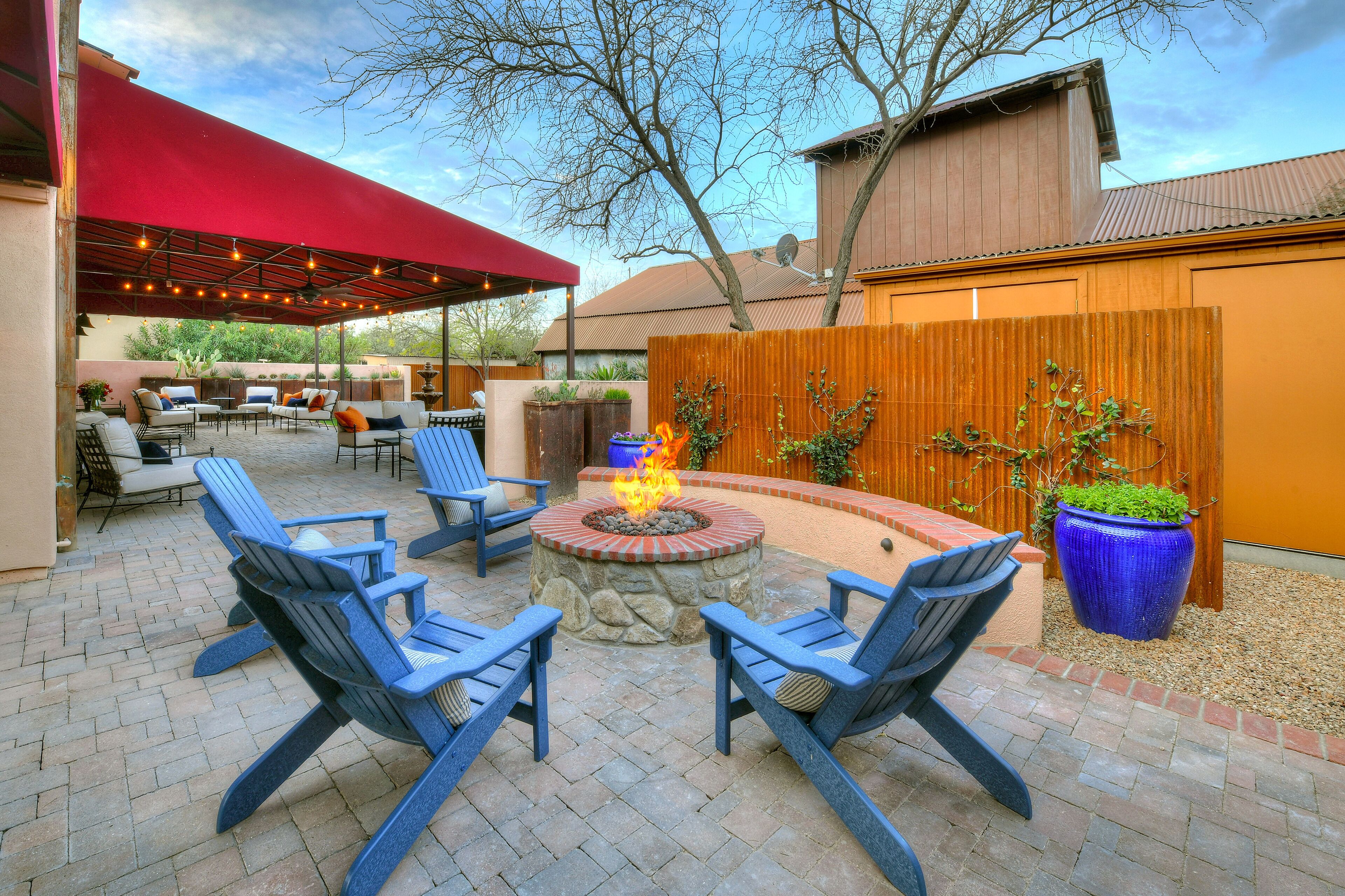 An outdoor patio with a fire pit, blue chairs, and a red canopy.