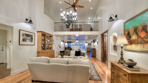 A spacious living room with a large sectional sofa, wooden flooring, a chandelier, and a painting on the wall.