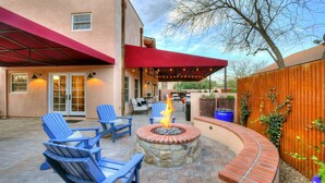 A patio with blue Adirondack chairs, a stone fire pit, and a red awning over the seating area.