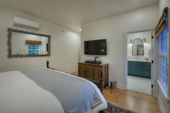 A bedroom with a bed, a dresser, a television, and a bathroom visible through an open door. - The Armory Park Inn (Tucson)