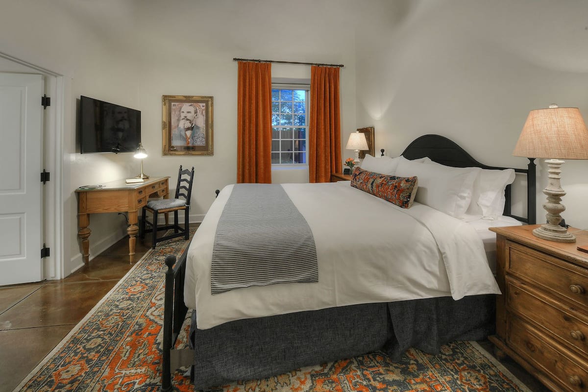 A bedroom with a large bed, a desk with a chair, a TV, and a window with curtains.