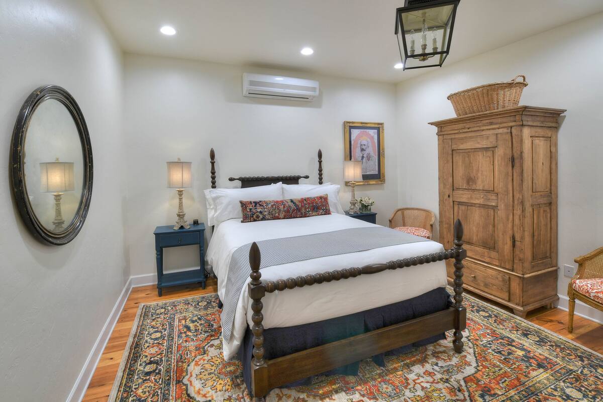 A bedroom with a four-poster bed, a wooden wardrobe, a nightstand, and a patterned rug.