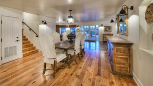 A dining area with a wooden table and chairs, a staircase, and a view of the outdoors.