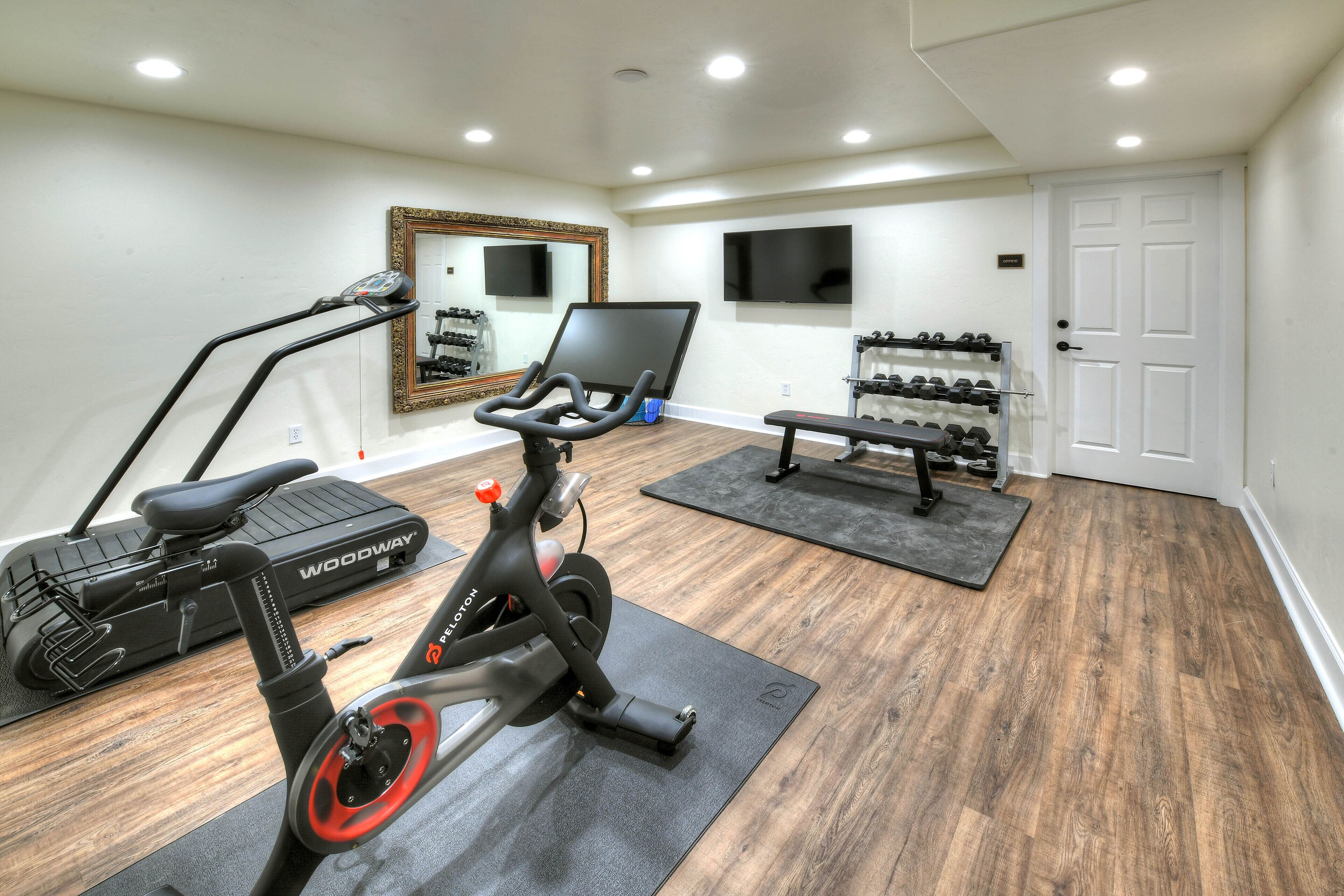 A home gym with a stationary bike, treadmill, weights, and a mirror.