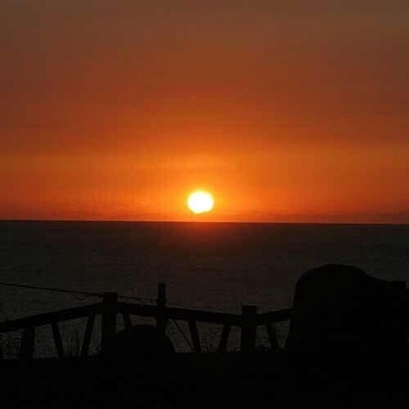 A sunset over the ocean with a wooden fence in the foreground.