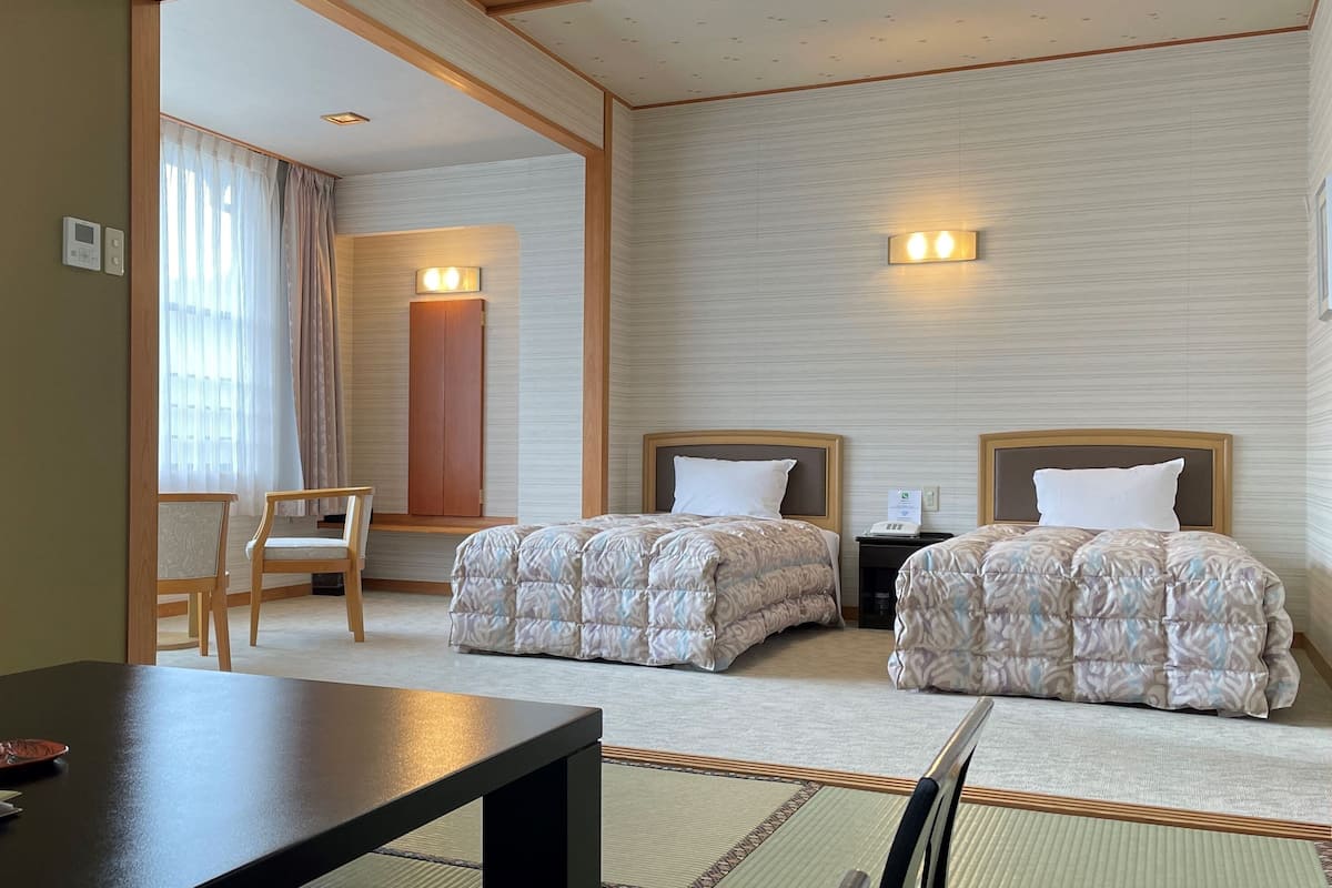 A hotel room with two beds, a desk, a chair, a mirror, and a window with curtains.