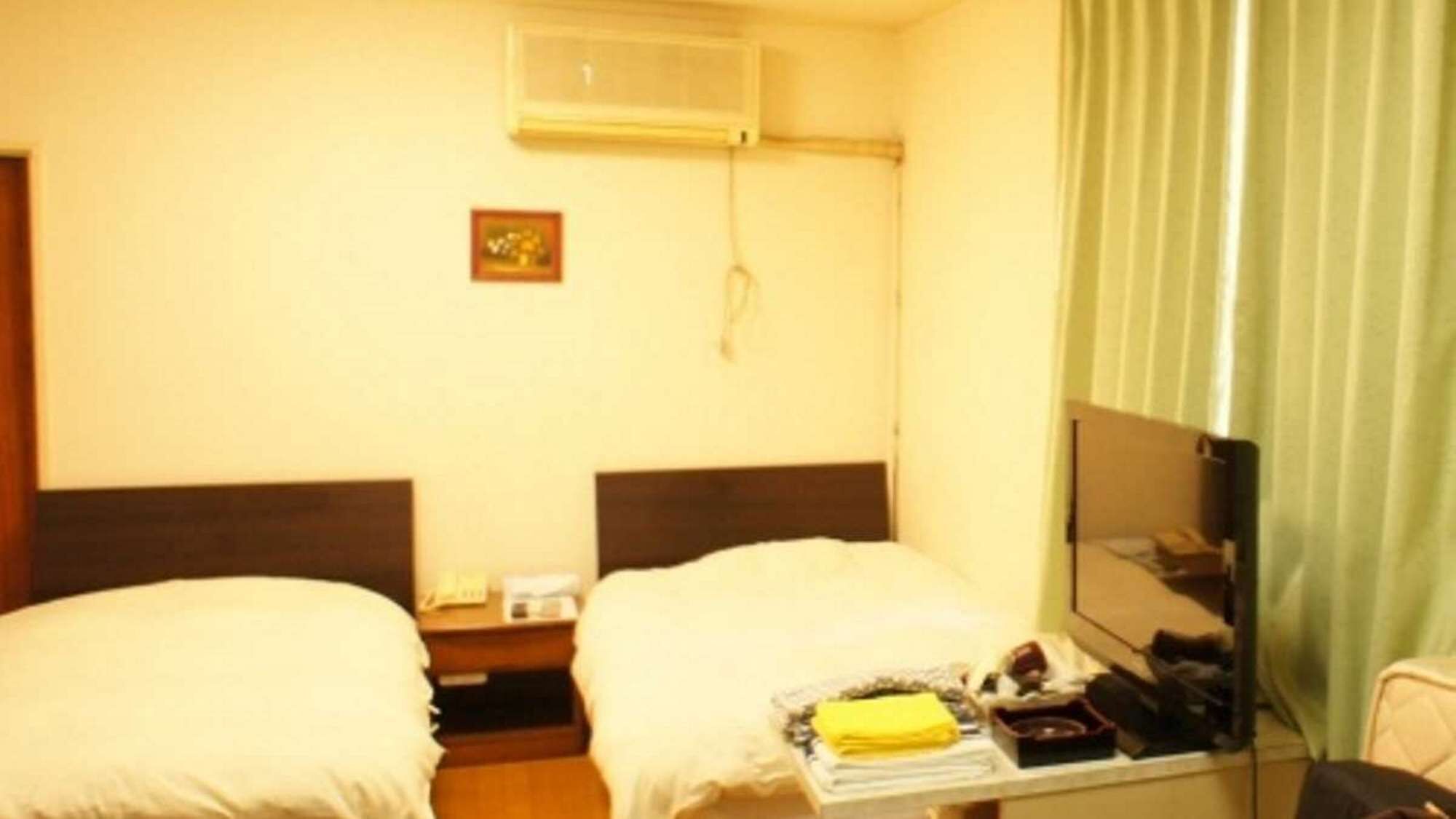 Habitación de hotel con dos camas, una mesita de noche, un espejo y una ventana con cortinas.