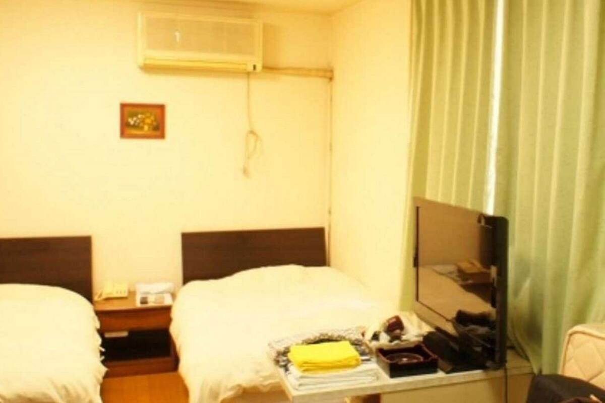 A hotel room with two beds, a bedside table, a mirror, and a window with curtains.