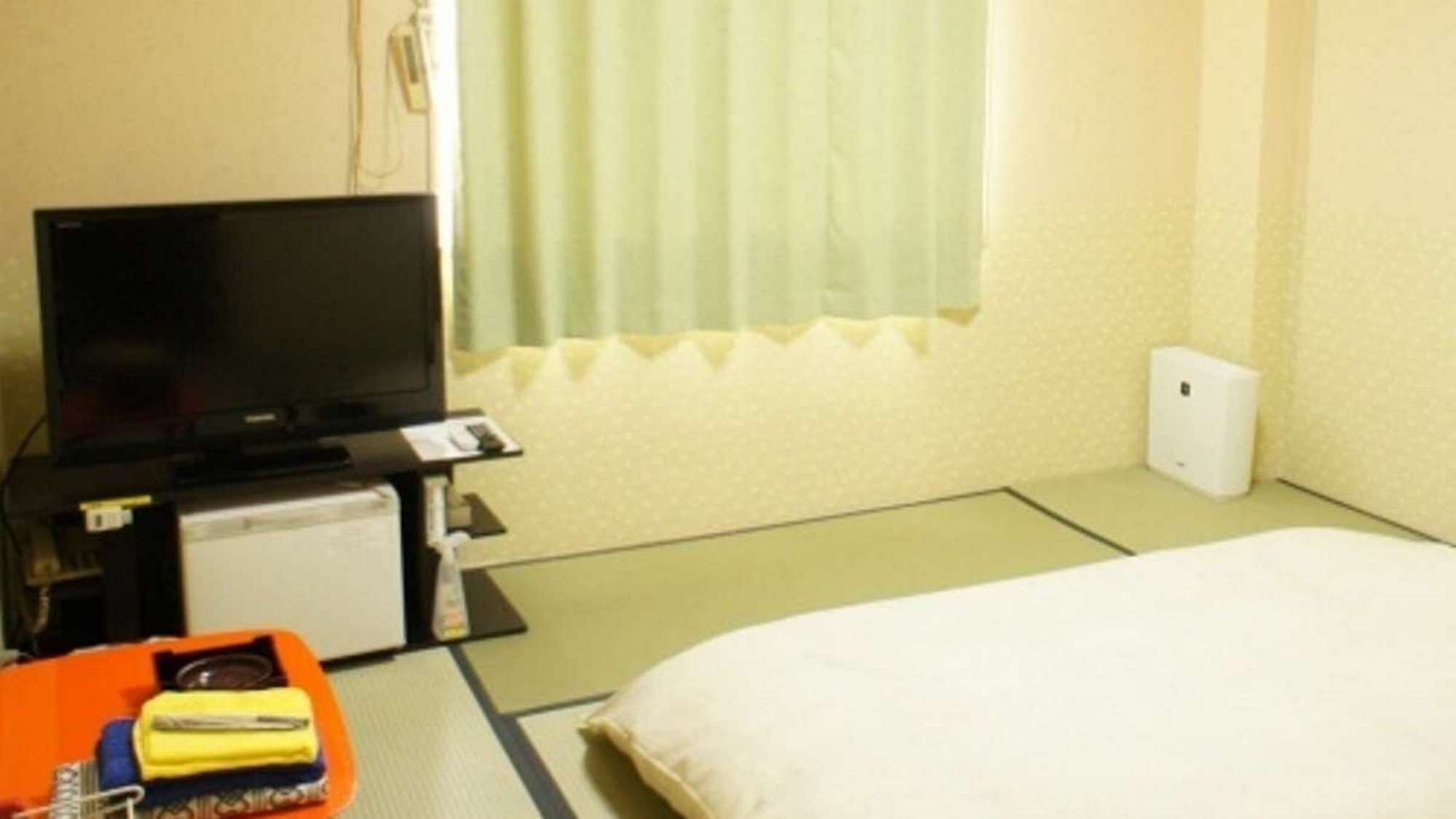 A hotel room with a bed, a television, a small desk with a computer, and a window with curtains.