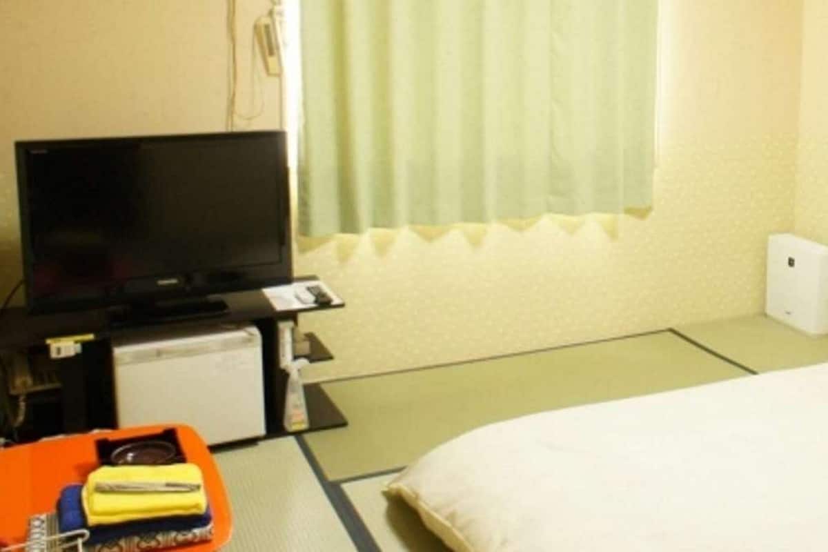 A hotel room with a bed, a television, a small desk with a computer, and a window with curtains.