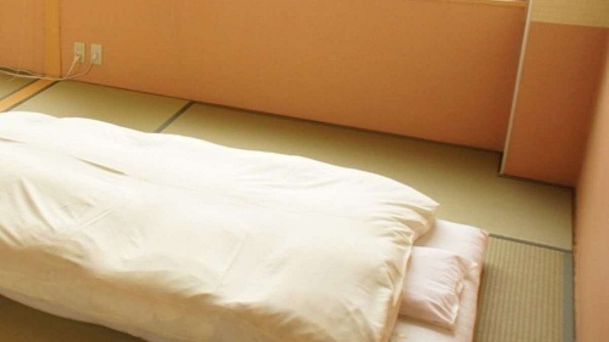 Una cama individual en una habitación con una pared naranja lisa y un suelo de baldosas.