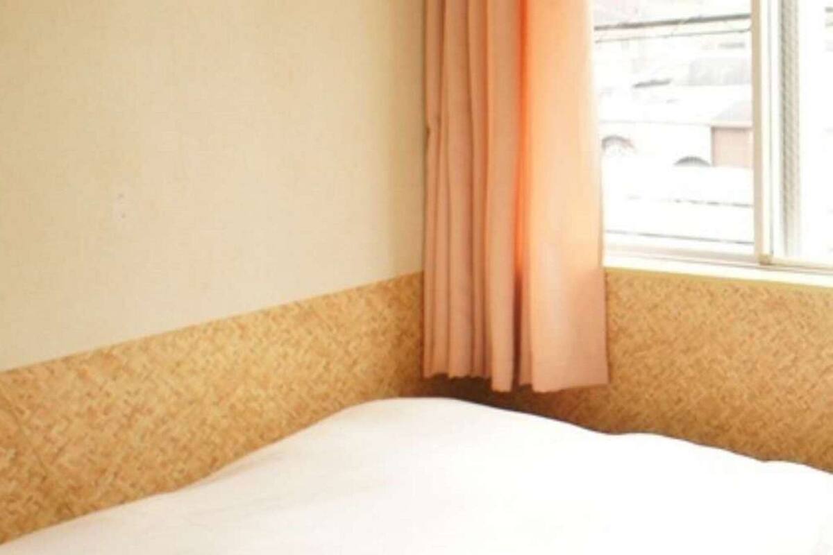 A hotel room with a bed, a window with curtains, and a wall socket.
