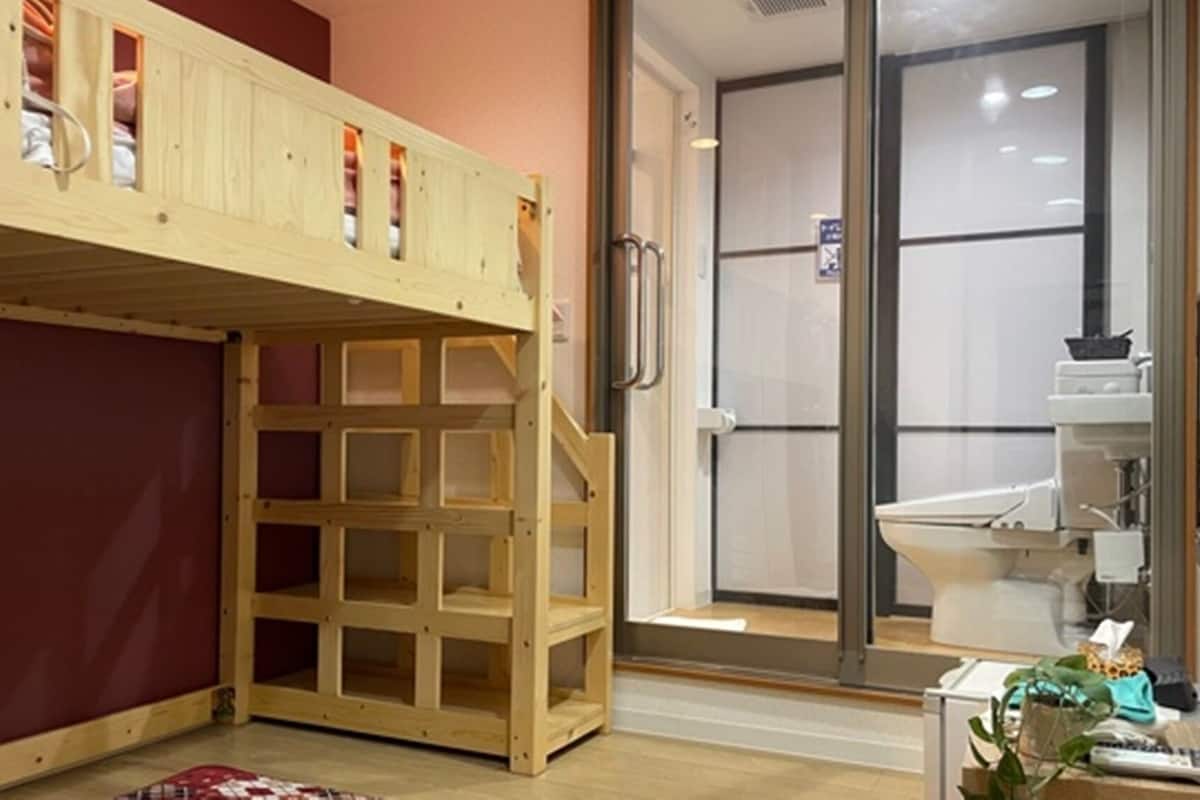 A room with a wooden bunk bed, a glass door leading to a bathroom, and a small table with a plant.