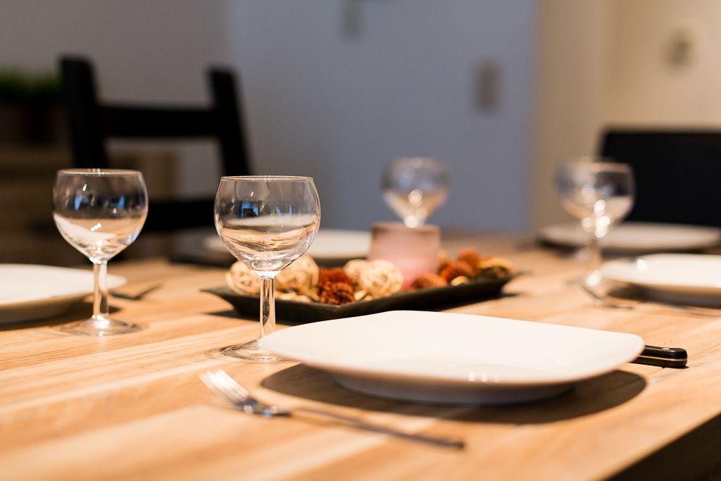 Una mesa de comedor dispuesta con copas de vino, platos y un recipiente pequeño con nueces.