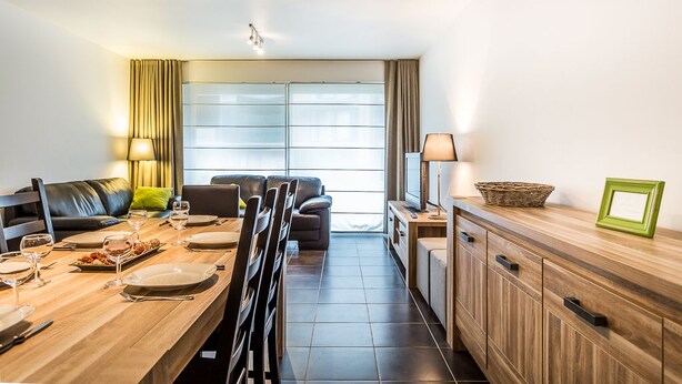 A modern living room with a dining area, a sofa, a TV, and a cabinet. - Santos Secundo GV01 (Koksijde)