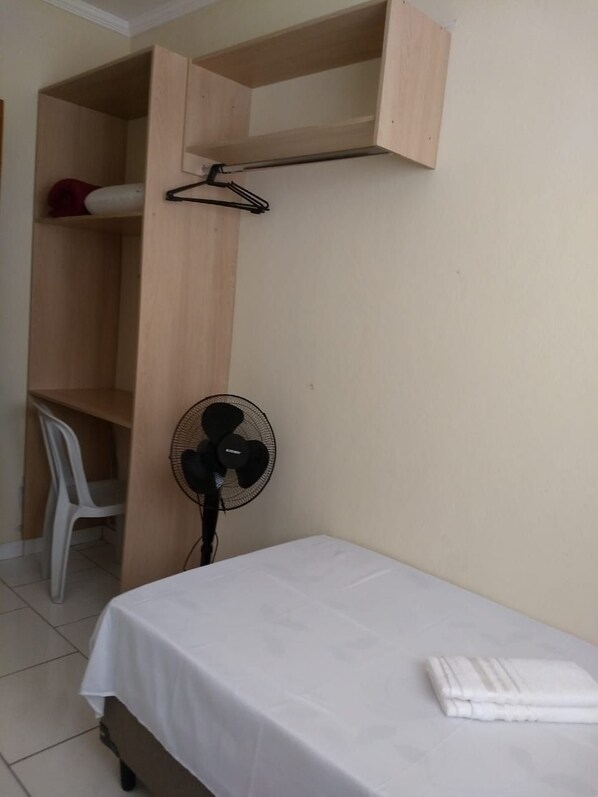A bedroom with a bed, a fan, a wooden wardrobe, and a white chair. - Acomodações Silvestre (Taubate)