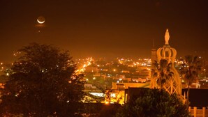 Un paisaje urbano nocturno con una luna creciente, edificios iluminados y una torre destacada con aguja.