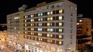 Un hotel de varios pisos con una fila de habitaciones en cada planta, un estacionamiento al frente y una entrada visible.
