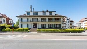 A two-story building with a balcony on the ground floor, a visible entrance, and a parking sign. - Etoilée GV04 (Koksijde)