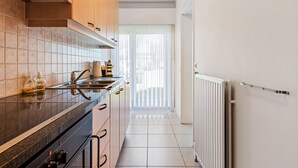 A modern kitchen with a black countertop, wooden cabinets, and a white tiled backsplash. - Etoilée GV04 (Koksijde)