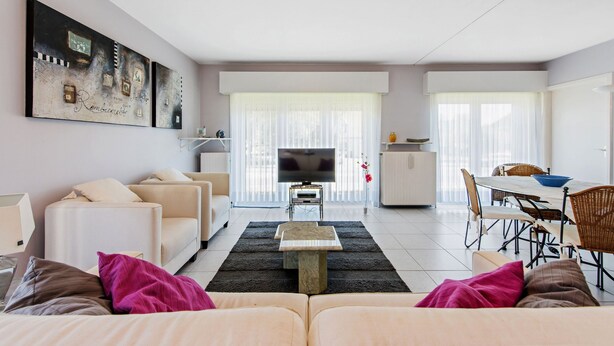 A modern living room with a sofa, a coffee table, a TV, and a dining area with chairs and a table. - Etoilée GV04 (Koksijde)
