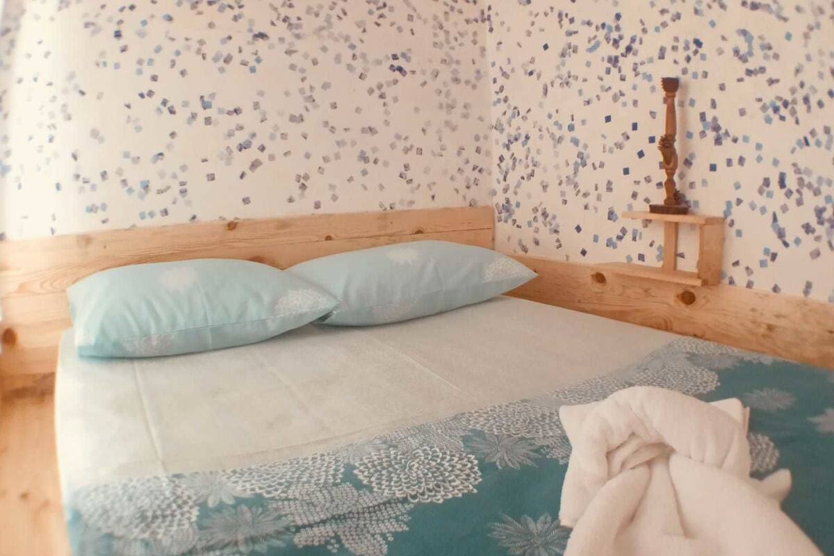 A bed with a wooden headboard, two light blue pillows, and a floral-patterned bedspread.