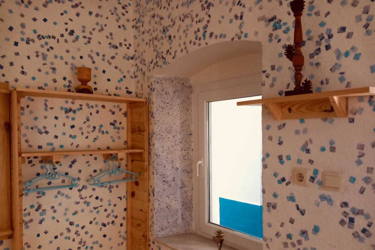 A room with a wooden shelf unit, a window with a blue view, and a wall with a mosaic pattern.