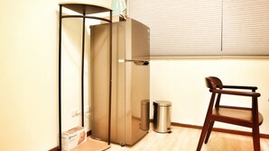 A compact kitchenette with a built-in refrigerator, a small trash bin, and a chair. - Good-Days Lovely Suite BRT Calligraphy Greenway (West Dist.)