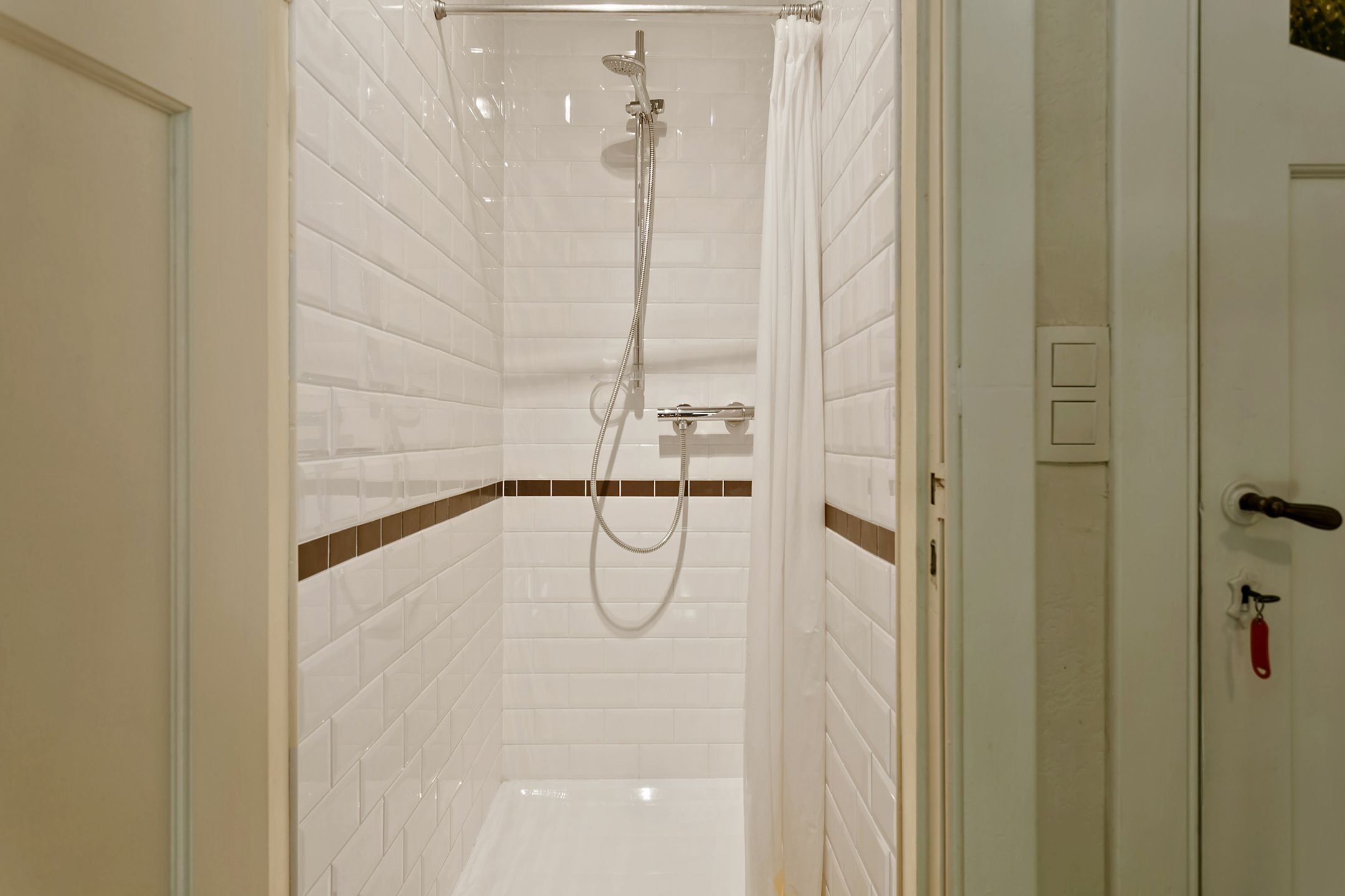 A shower area with white tiled walls and a showerhead.