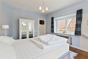 A bedroom with a bed, a dresser, a mirror, a window with curtains, and a radiator. - Zeehuis (Koksijde)