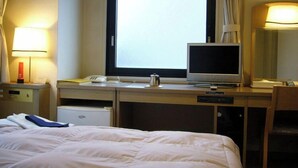 Hotellihuone, jossa on sänky, työpöytä tietokoneella, puhelin ja ikkuna, jossa on verhot.