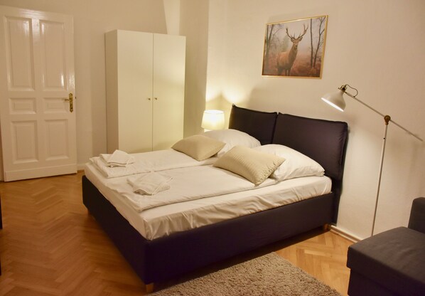 A bedroom with a bed, a wardrobe, a lamp, and a painting on the wall.