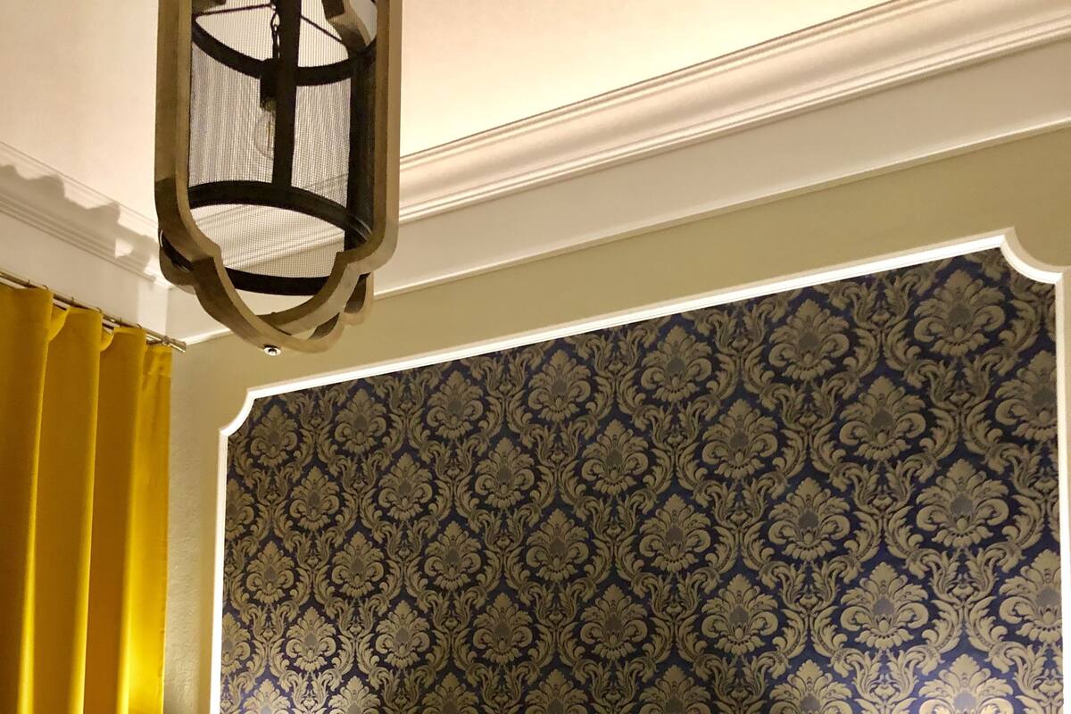 Una cama con cabecera oscura, papel tapiz estampado y cortinas amarillas.