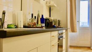 A kitchen with white cabinets, a black range hood, and a window with curtains. - Aparthotel Thüringer Hof (Berlin)