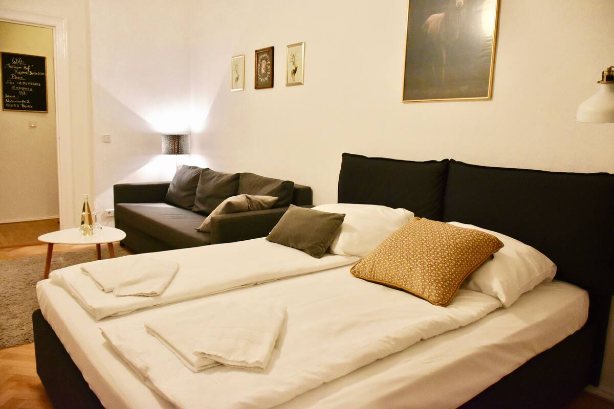 Habitación de hotel con cama, sofá, una mesita y una lámpara de pared.