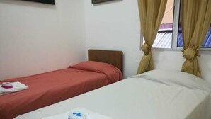 A hotel room with two beds, one with a red bedspread and the other with a white bedspread. There is a window with beige curtains, a framed picture on the wall, and a white towel with a blue logo on the bed. - Lindo Apartamento en el Centro de Panama (Panama City)