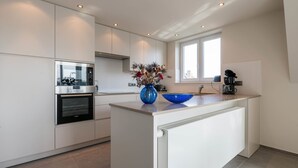 Una cocina moderna con armarios blancos, horno empotrado, cafetera y un florero con flores secas en la isla.